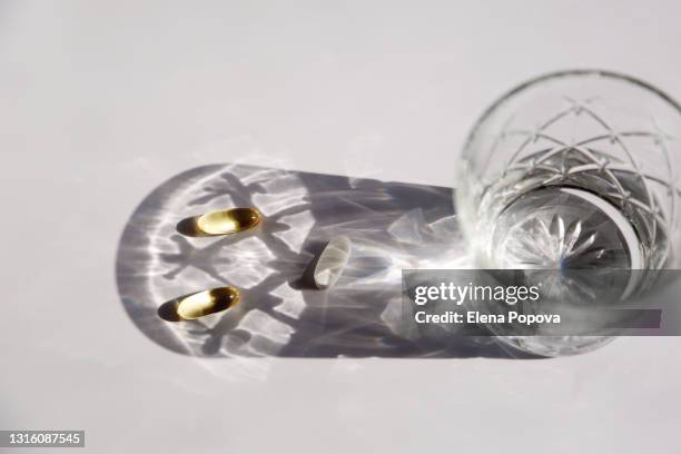 two omega-3 capsules and magnesium pill next the glass of water - calcita fotografías e imágenes de stock