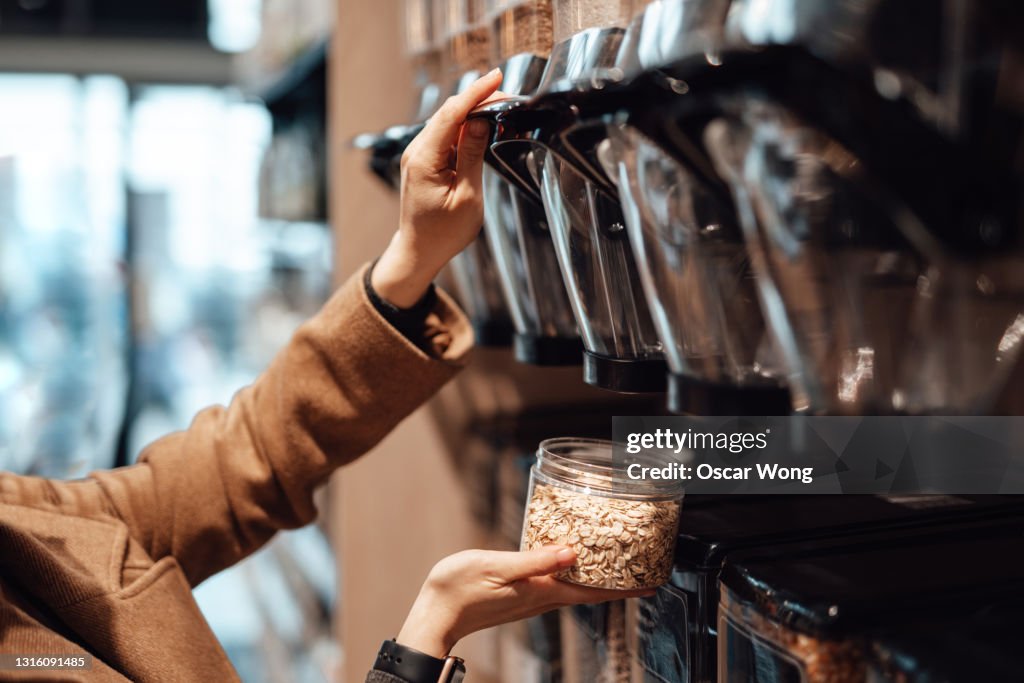 Woman in organic whole foods refilling store dispensing oats into a reusable container.