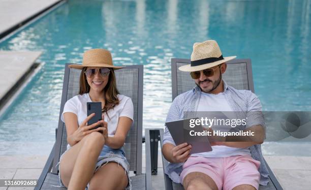 glückliches paar entspannen am pool im urlaub beim überprüfen der sozialen medien - tablet paar sommer stock-fotos und bilder