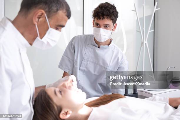 zahnärzte arbeiten an den zähnen junger frau in der zahnarztpraxis - zahnarzthelfer stock-fotos und bilder