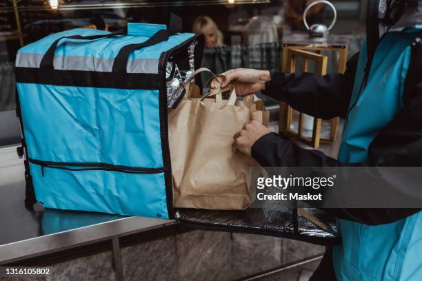 midsection of delivery man putting package order in backpack outside deli store - gig economy stock pictures, royalty-free photos & images