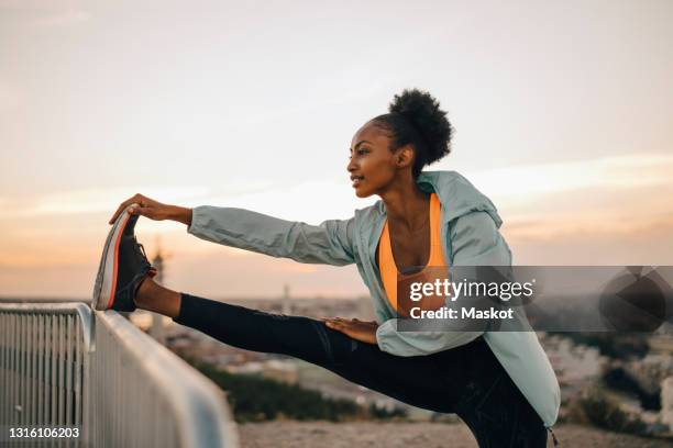sportswoman doing stretching exercise against sky during sunset - stretching foto e immagini stock