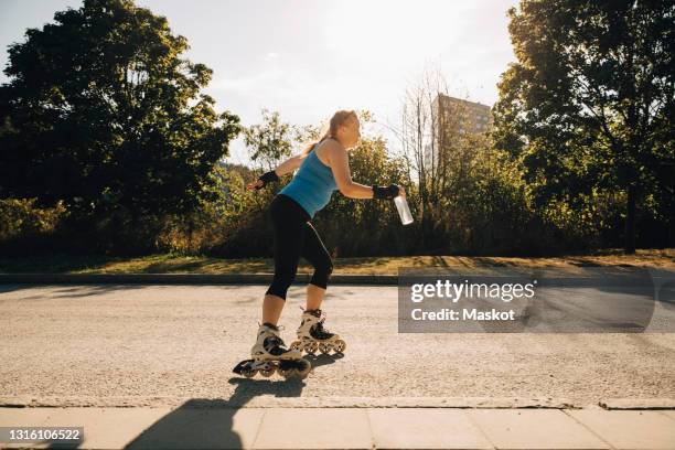 female athlete roller skating on street during sunny day - skaten stockfoto's en -beelden