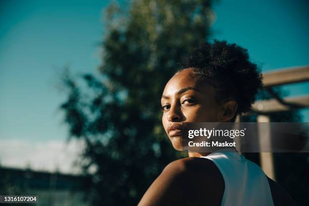 portrait of female athlete looking over shoulder on sunny day - women in sport stock-fotos und bilder