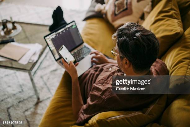 high angle view of male entrepreneur working on laptop in living room - laptop couch stock pictures, royalty-free photos & images