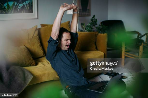 businessman stretching hands while sitting with laptop in living room - yawning is contagious imagens e fotografias de stock