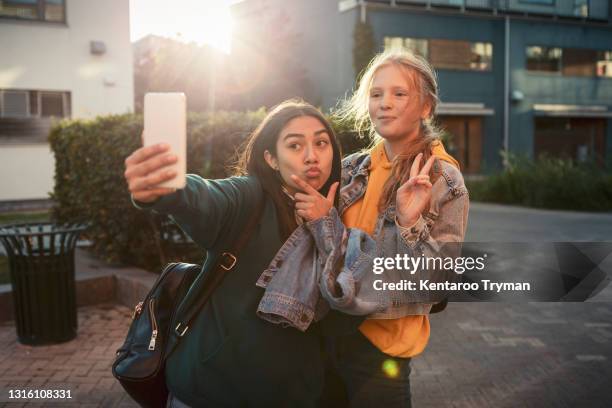 female friends gesturing while taking selfie over smart phone on footpath - signaling pathways stock-fotos und bilder