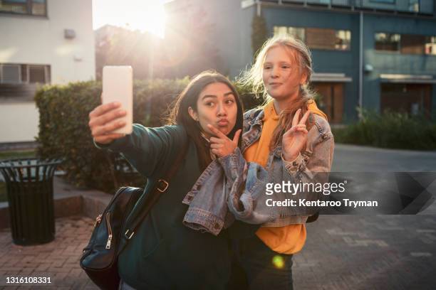 female friends gesturing while taking selfie over smart phone on footpath - adolescents selfie ストックフォトと画像