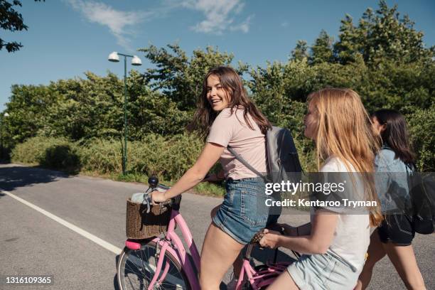 female teenagers cycling on street during sunny day - 14 year old brunette girl stock pictures, royalty-free photos & images