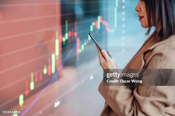 businesswoman analysing and checking stock market over smartphone in downtown financial district - beurskoers tabel stockfoto's en -beelden