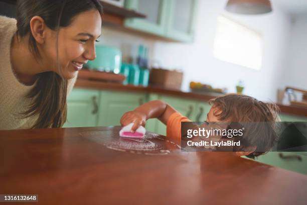 shot of an adorable little boy helping his mother clean the kitchen counter at home - tidy room stock pictures, royalty-free photos & images
