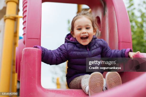 una niña de 2-3 años que se desliza fuera del tobogán es muy feliz, emoción positiva - área de juego fotografías e imágenes de stock
