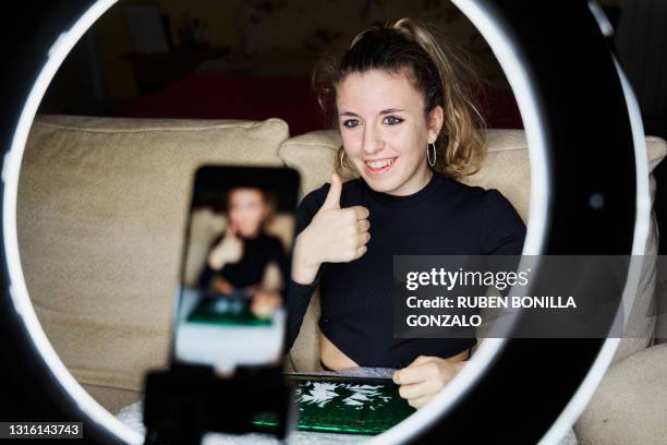 young smiling teenager girl influencer with her thumb up filming with her mobile phone through a led lighting ring. - filming tutorial stock pictures, royalty-free photos & images