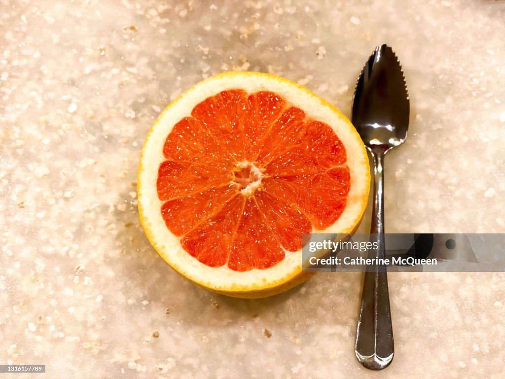 Sliced half of fresh grapefruit beside serrated spoon