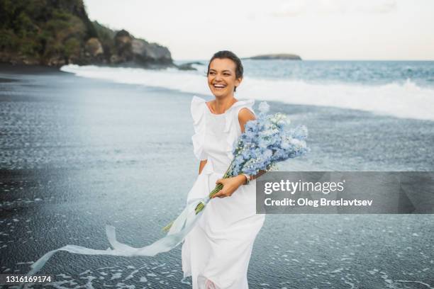 bride in white wedding dress having fun and laughing in splashing ocean waves and getting wet. trash the dress style - ranunculus wedding bouquet stock pictures, royalty-free photos & images
