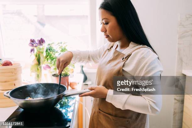 young beautiful asian woman preparing a tasty meal in her kitchen - hot filipina women stock pictures, royalty-free photos & images