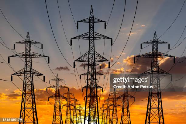 high voltage towers at sunset background. power lines against the sky - producción de combustible y energía fotografías e imágenes de stock