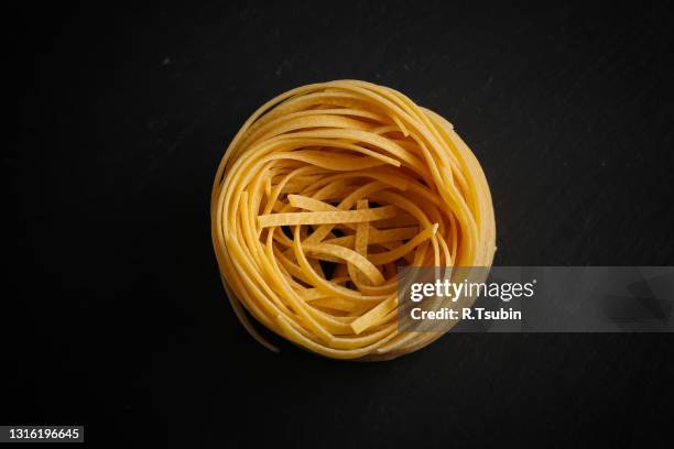 fettuccine pasta nest on black stone background - フェットチーネ ストックフォトと画像