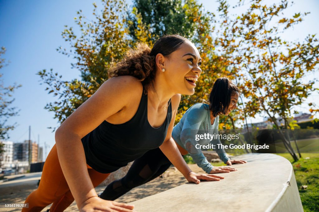 Cheerful women doing push-ups on retaining wall at park