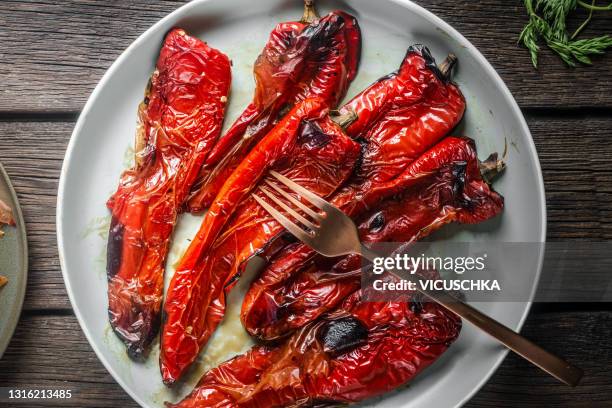 close up of roasted red pepper with fork on white plate. rustic wooden background - roasted pepper stock-fotos und bilder