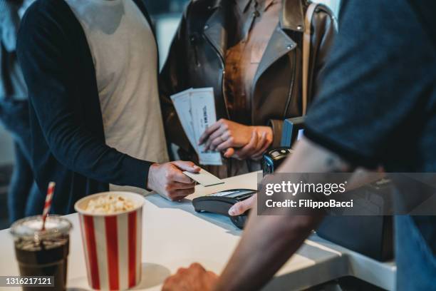 millennial man is paying with a contactless credit card at the movie theater's bar counter - theatre program stock pictures, royalty-free photos & images