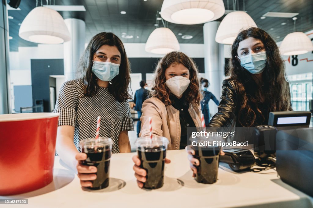 Three adolescent friends are at the bar counter, buying popcorn and drinks