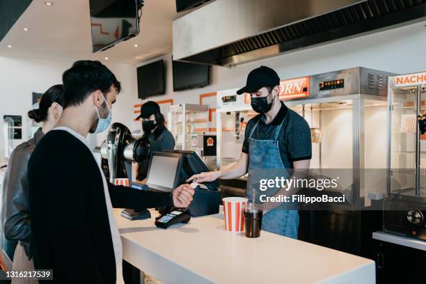 millennial man is paying with a contactless smart watch at the movie theater's bar counter - theatre program stock pictures, royalty-free photos & images