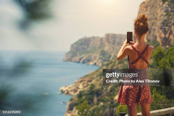 rear view young woman holding cellphone taking photo of beautiful nature - parte del cuerpo humano fotos fotografías e imágenes de stock