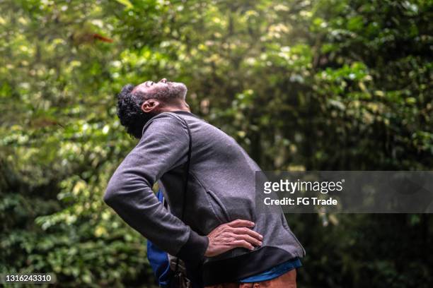 rijpe mens die rugpijn ervaart of zich in een bos uitrekt - back stretch stockfoto's en -beelden