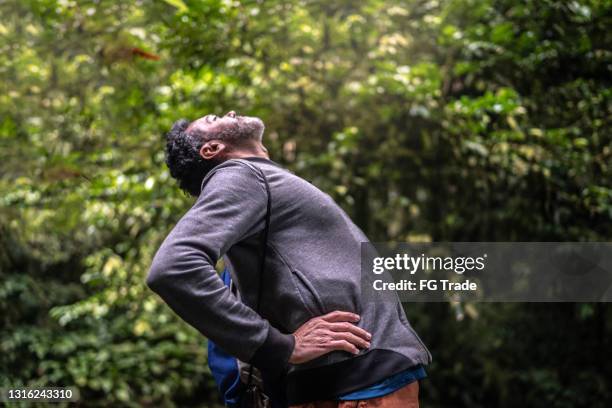 mature man experiencing back pain or stretching in a forest - hernia stock pictures, royalty-free photos & images