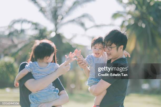 aziatische chinese jonge familie met tweelingbaby's hoge vijf die pret hebben die van het spelen in openbaar park in de ochtend genieten - asian twins stockfoto's en -beelden