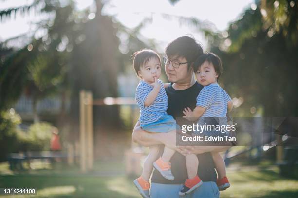 aziatische chinese vader die met zijn tweelingbabyjongens in openbare parkochtend bindt - asian twins stockfoto's en -beelden