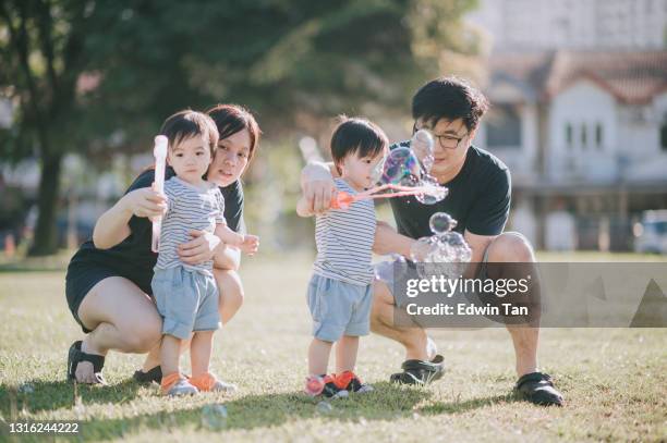 aziatische chinese jonge familie met tweelingbabyjongens die bij openbaar park met bellenstok in de ochtend spelen - asian twins stockfoto's en -beelden