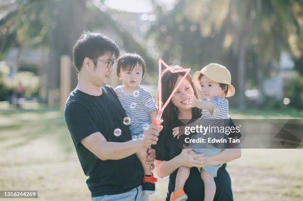 aziatische chinese jonge familie met tweelingbabyjongens die bij openbaar park met bellenstok in de ochtend spelen - asian twins stockfoto's en -beelden