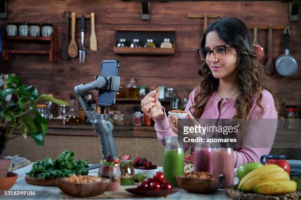 hispanische junge frau vlogging gesunde smoothies rezepte in einer rustikalen küche - fruit smoothie instagram stock-fotos und bilder