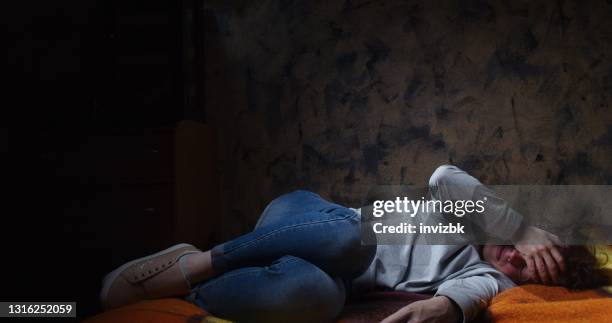 distressed woman is lying in fetal position on the sofa in dark room - hugging knees stock pictures, royalty-free photos & images