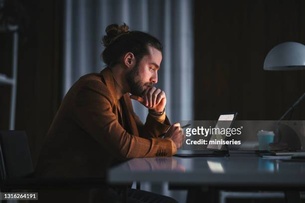 homme pensif travaillant sur l’ordinateur portatif dans le bureau - recherche photos et images de collection