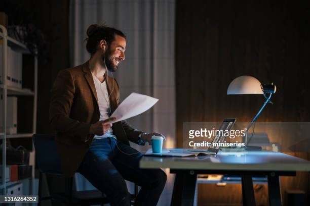 happy man having video call from dark home office - remote location stock pictures, royalty-free photos & images