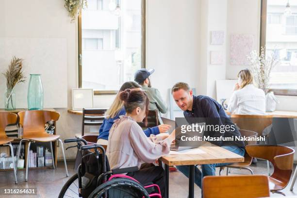 Asian young female entrepreneur in a wheelchair having a business conversation with her team in a local space