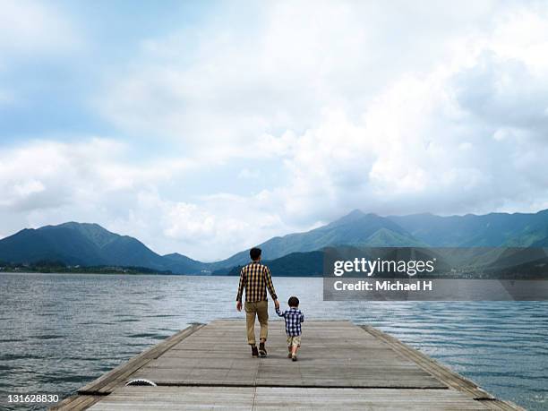 father and son on a pier overlooking the lake - father and son walking stock pictures, royalty-free photos & images