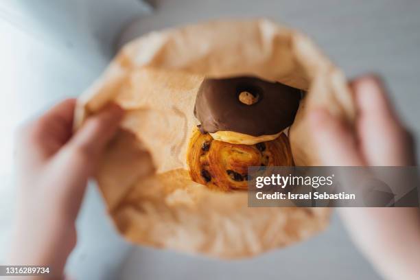 view from above of an unrecognizable girl holding a paper bag full of buns. you can see the buns inside. - breakfast to go stock-fotos und bilder