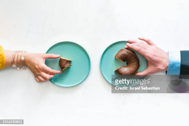 view from above of a woman's hand and a man's hand holding up two different sized pieces of a chocolate bun. concept of labor inequality. - unfairness photos et images de collection