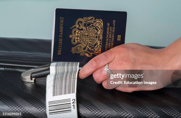 In this photo illustration, a new dark blue colored British passport held in a travellers hand with holiday suitcase.