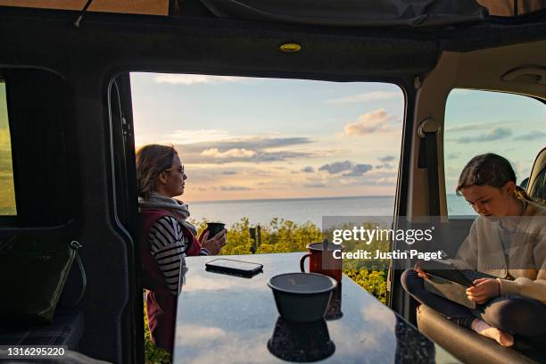 a woman takes in the view by her campervan. her daughter sits inside on her digital tablet - rv beach stock pictures, royalty-free photos & images