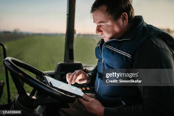 uomo che usa tablet digitale e seduto in un trattore - tractor foto e immagini stock