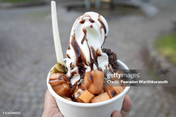 close-up and top outdoor view at white frozen yogurt serve with topping with melon, kiwi and chocolate in paper white cup, on hand. - gefrorener joghurt stock-fotos und bilder