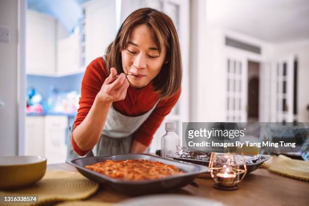 young pretty asian woman tasting a dish of pasta she prepared while serving food on the table at home - vivere semplicemente foto e immagini stock