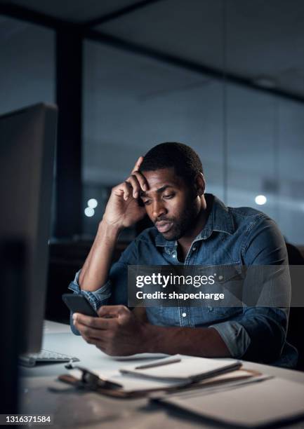 ontsproten van een jonge zakenman die beklemtoond kijkt terwijl het gebruiken van een smartphone tijdens een recente nacht in een modern bureau - hundreds of gitanjali gems workers protest over uncertainty of employment stockfoto's en -beelden