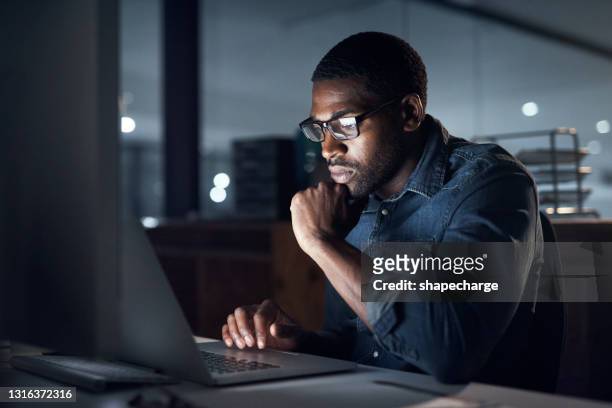 scatto di un giovane uomo d'affari che usa un laptop durante una tarda notte in un ufficio moderno - black man laptop foto e immagini stock
