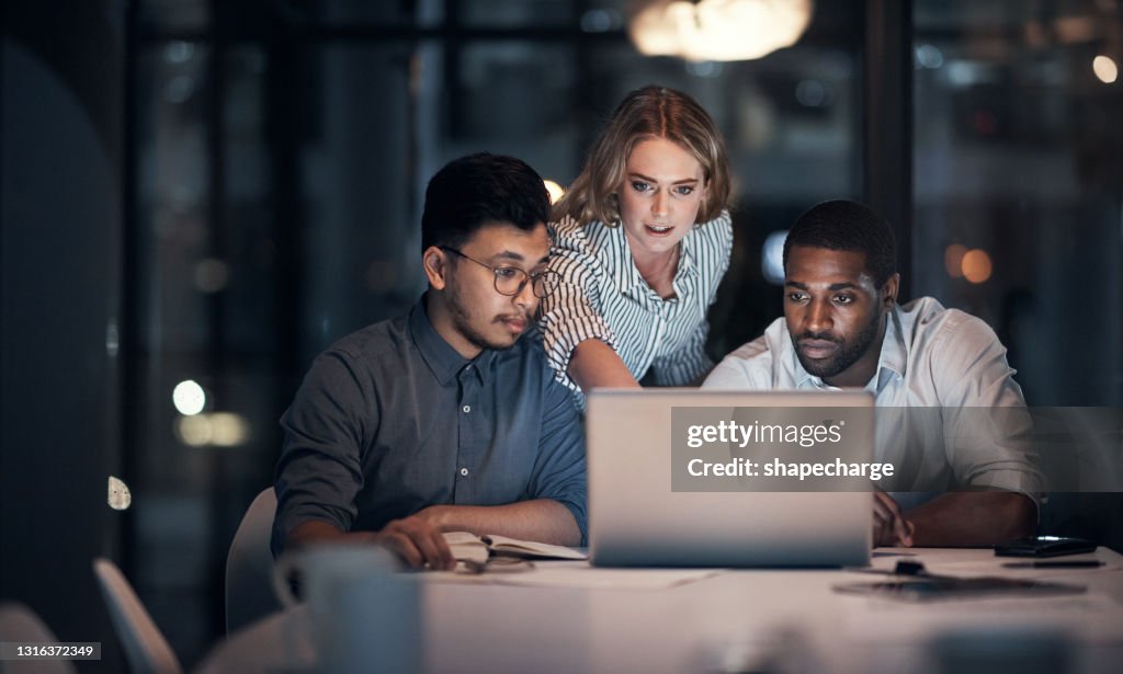 Shot of a team of young businesspeople using a laptop during a late night meeting in a modern office
